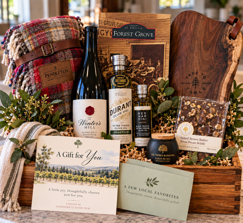Hand-curated wooden gift box with a plaid blanket, serving board, bottled goods, treats, greenery, and Consider It Done cards.